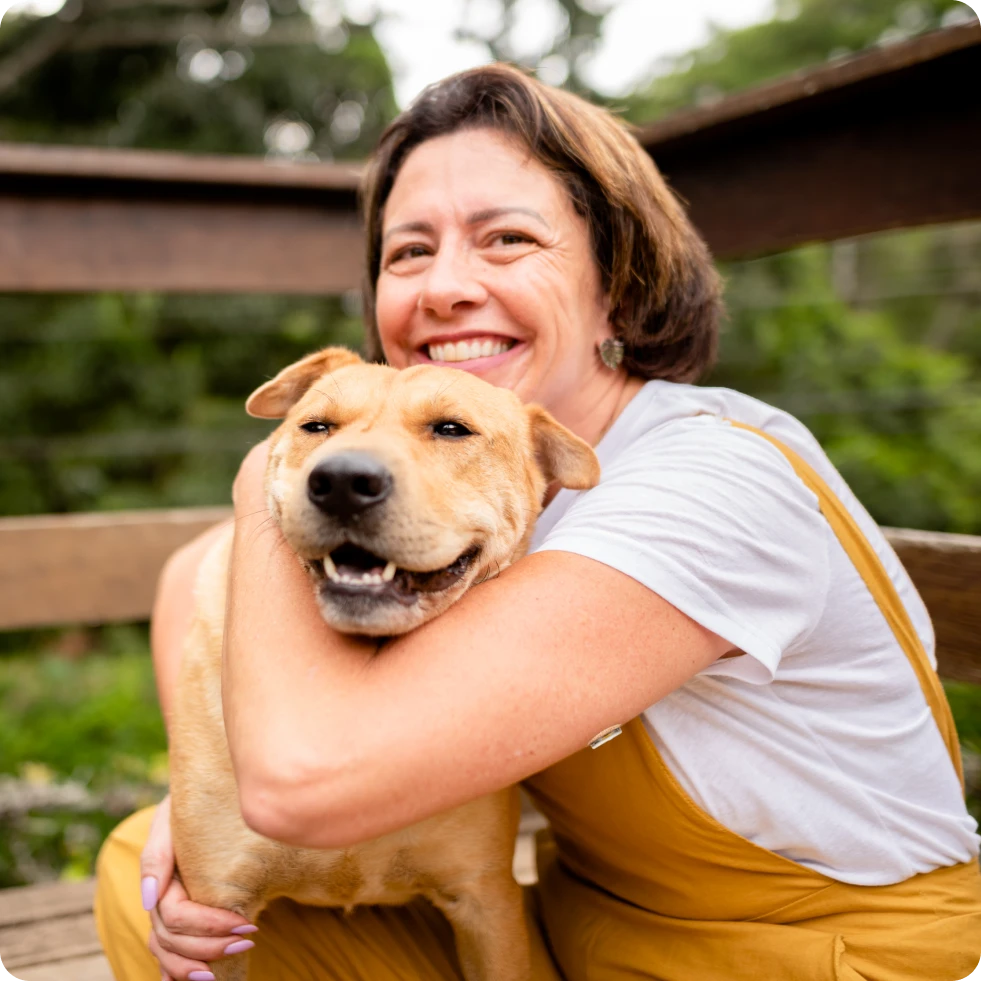 A woman hugging her dog and smiling.
